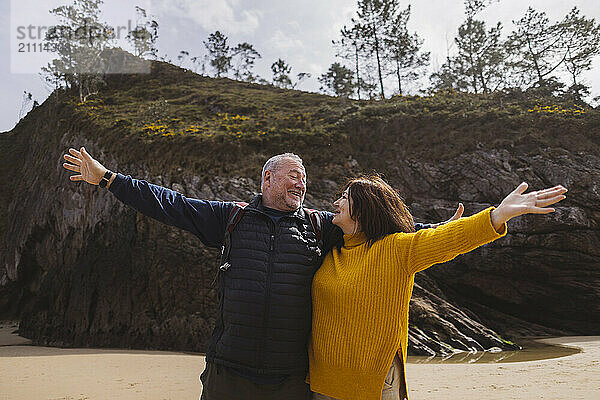 Carefree senior couple with arms outstretched standing at beach