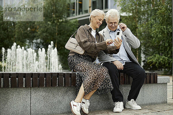 Senior couple sitting and using smart phone at street