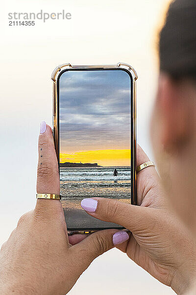 Woman holding smart phone and taking photo at beach