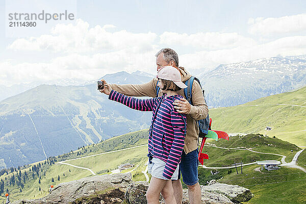 Father with daughter taking selfie on smart phone at mountain peak