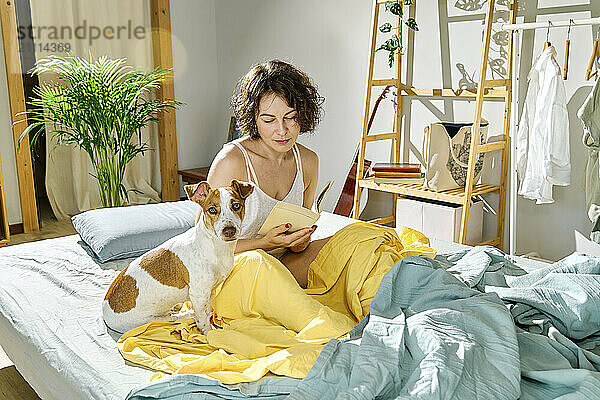 Woman reading book near Jack Russell Terrier dog on the bed at home