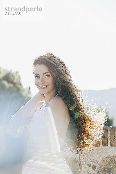 Smiling woman with long hair standing near stone wall