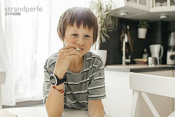 Cute boy eating slice of apple in kitchen