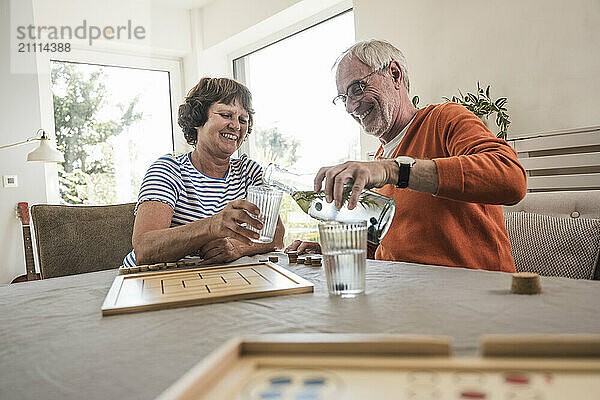 Senior man sitting near table and pouring water in glass for wife at home