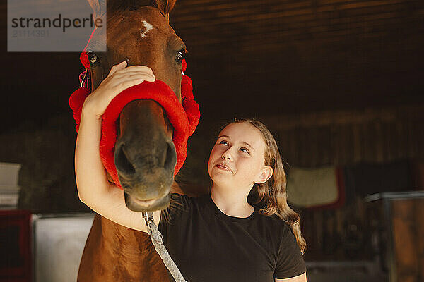 Smiling girl with horse in barn