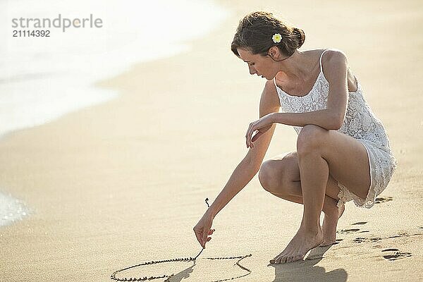 Young woman making heart shape on wet sand at beach