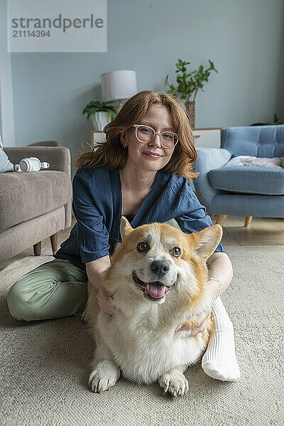 Smiling woman with Welsh Corgi dog sitting at home