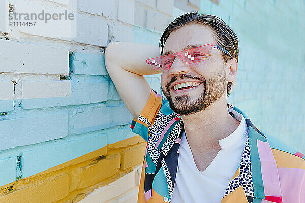 Happy man wearing eyeglasses and leaning on brick wall