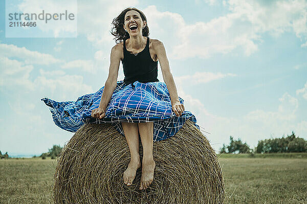 Carefree woman sitting on bale of hay in field