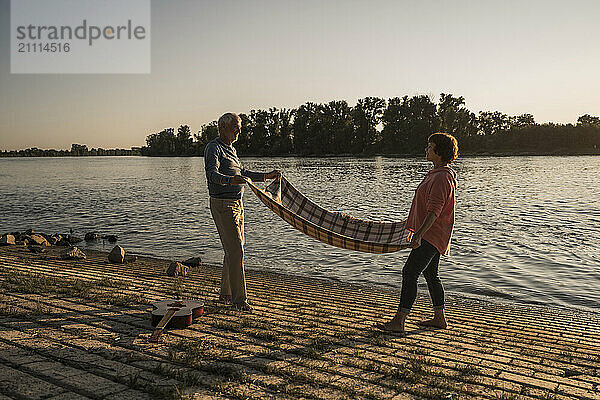 Senior couple holding picnic blanket at riverbank