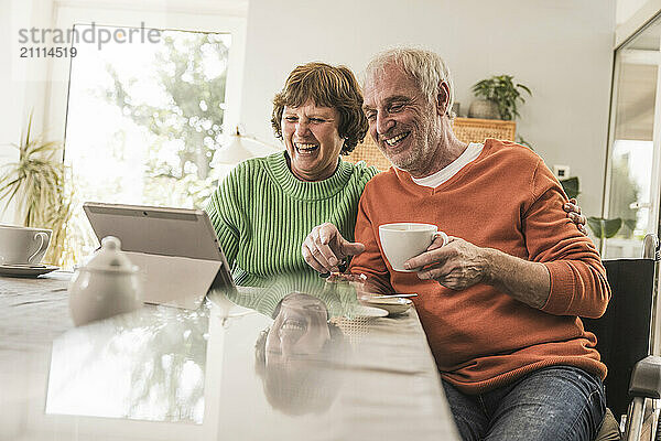 Laughing woman with husband talking on video call using tablet PC at home