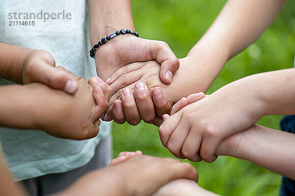 Close-up of children's hands stacked together in a gesture of teamwork and unity on a blurred green background.