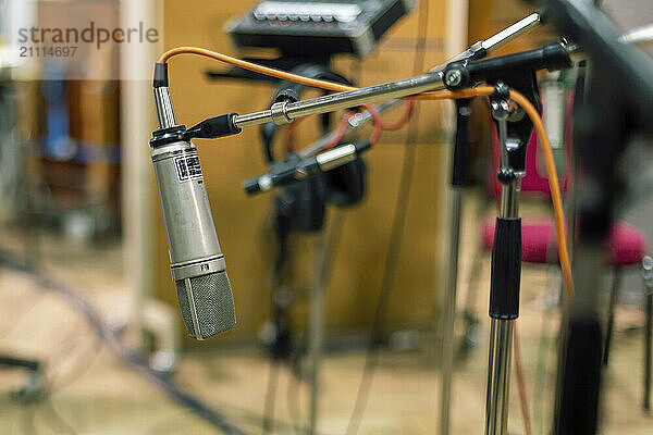 Studio microphone with a pop filter set against a blurred background of musical equipment.