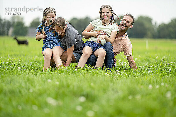 Smiling family having fun outdoors  with two children playing piggyback with their parents on a lush green field.