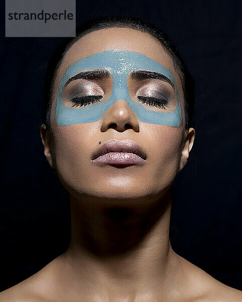 Close-up portrait of a woman with turquoise facial paint against a black background.