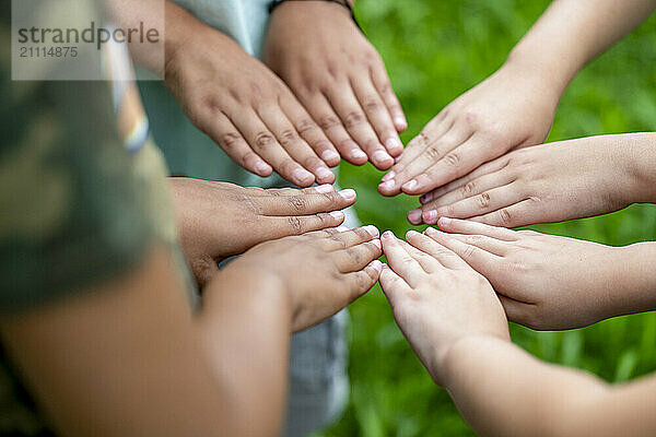 A group of people placing their hands together in a circle on a grassy background  symbolizing unity and teamwork.