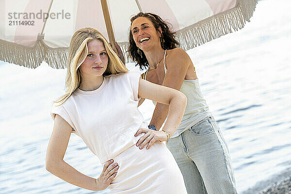 Two women smiling under a beach umbrella with the sea in the background.