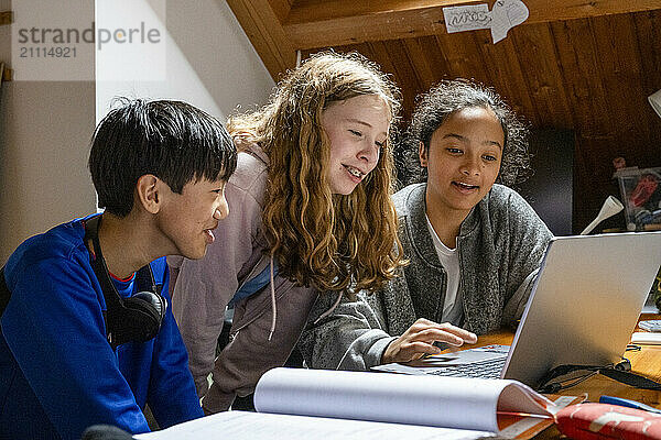 Three teenagers engrossed in an educational activity on a laptop in a cozy attic room.