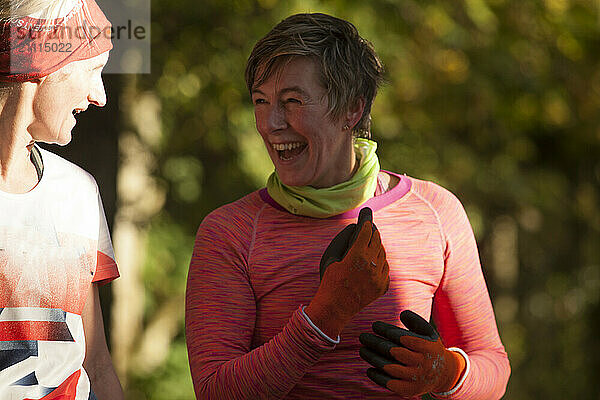 Smiling woman in pink running attire talking with a runner in a white shirt against a blurred autumn backdrop.