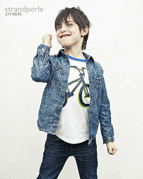 Smiling boy in a denim jacket posing with a fist pump gesture against a white background.