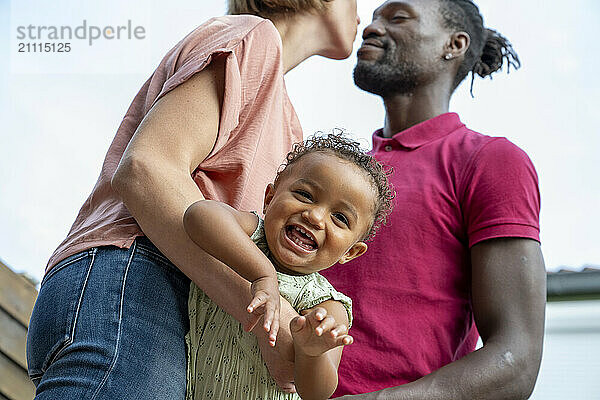 A joyful toddler laughs while being held by her parents  showcasing a heartwarming family moment.