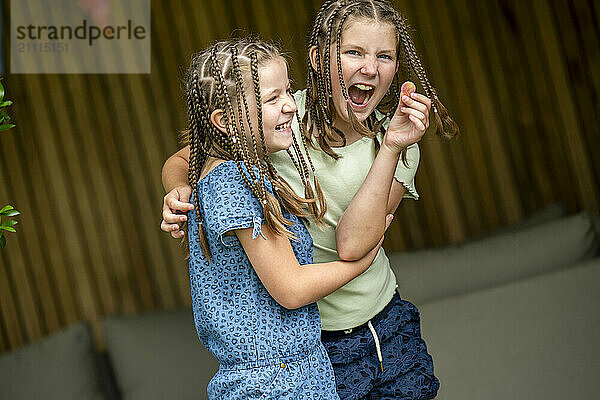 Two girls with braided hair share a joyful hug while laughing outdoors.