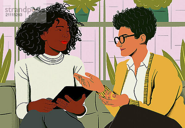 Two women engage in a friendly conversation while one holds a tablet in a cozy room with plants.