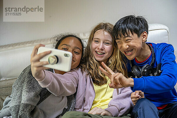 Three cheerful kids taking a selfie on a couch  with one flashing a peace sign.