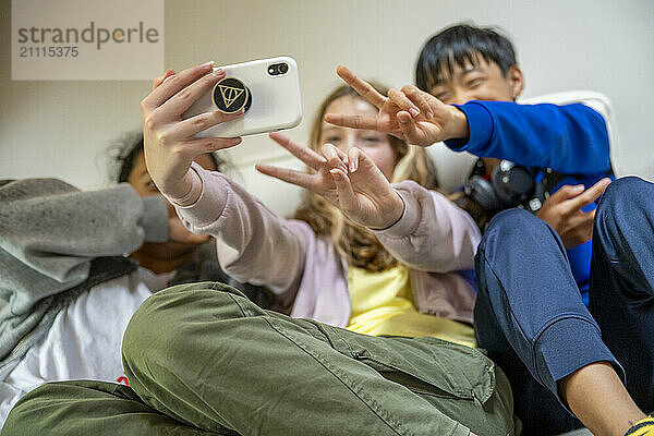 Three children take a selfie with a smartphone  making playful gestures and smiling.