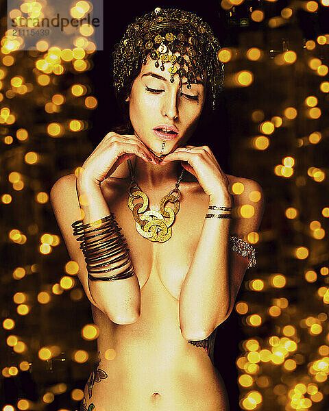 Elegant woman with decorative headpiece and jewelry posing against a backdrop of golden lights