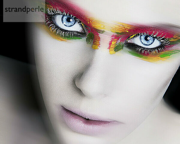 Close-up portrait of a person with vibrant  multicolored makeup around their eyes  highlighting striking blue irises.