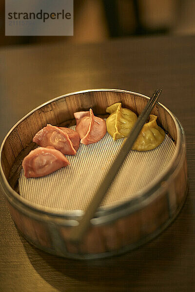 Dim sum in a bamboo steamer on a wooden table with chopsticks resting on top.