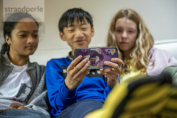 Three teenagers are engrossed in a smartphone game  sitting closely together on a comfortable couch.