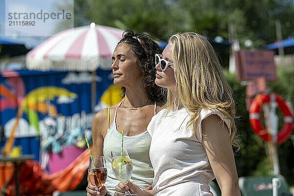 Two women enjoying drinks outdoors at a colorful  festive venue on a sunny day.