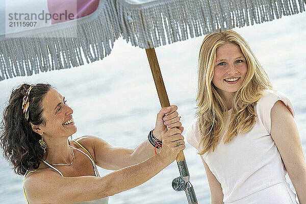 Smiling woman and teenage girl holding a beach umbrella together.