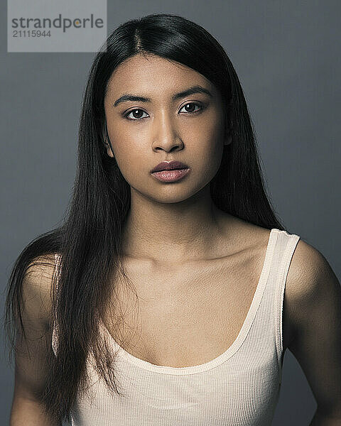 Close-up portrait of a young woman with long hair and neutral expression against a gray background.