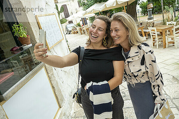 Two women smiling and taking a selfie together outside a restaurant.