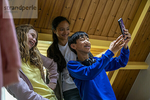 Smiling teenagers taking a selfie together with a smartphone indoors under a wooden ceiling.