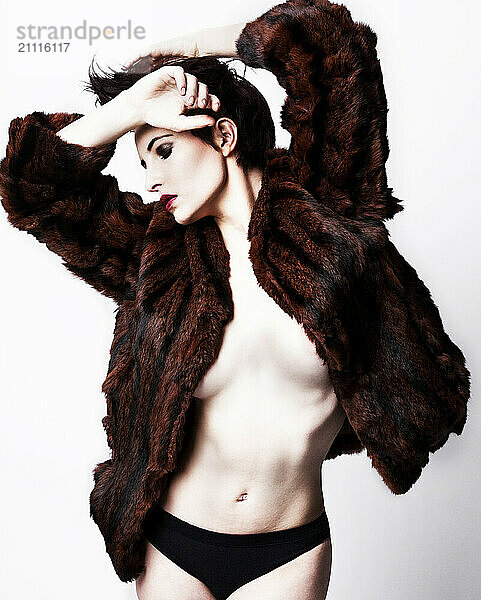 Fashion model posing in a dark brown fur coat with a dramatic pose against a white background.