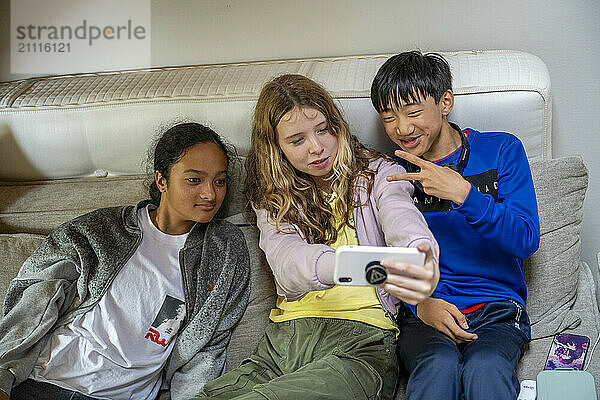 Three teenagers taking a selfie on a couch with one flashing a peace sign.