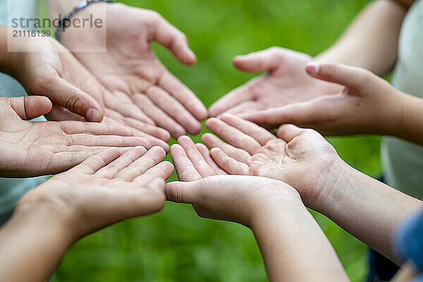 Open hands of several people extended towards each other against a green blurred background.