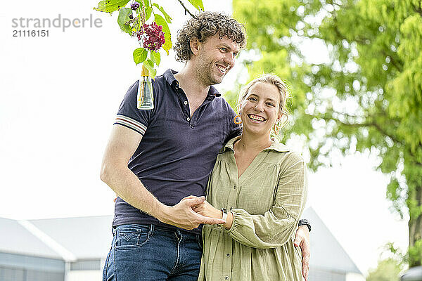 Smiling couple walking outdoors with a backdrop of trees and a clear sky  holding hands and enjoying each other's company.