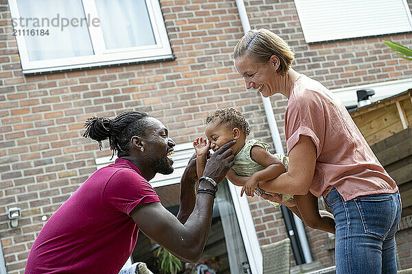 Smiling family playing with a toddler outside their home.