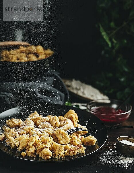 Kaiserschmarrn auf einem schwarzen Teller  wird mit Zucker bestreut  dunkler Hintergrund