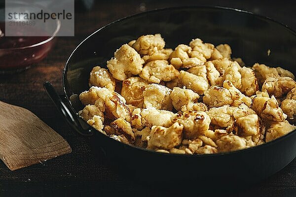 Kaiserschmarrn in einer Pfanne  Nahaufnahme mit braunem Holzlöffel und Marmelade auf dunklem Hintergrund