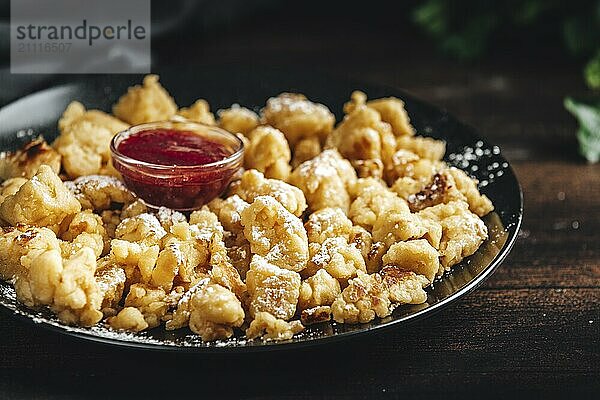 Kaiserschmarrn auf einem schwarzen Teller mit Puderzucker  kleine Schüssel mit roter Marmelade  dunkler Hintergrund