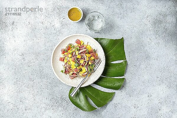 Tropischer hawaiianischer Thunfisch Mango Salat auf weißem Teller auf tropischem Monstera Blatt