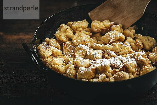 Kaiserschmarrn in einer Pfanne mit Zucker bestäubt und Holzspatel  Nahaufnahme  dunkler Hintergrund