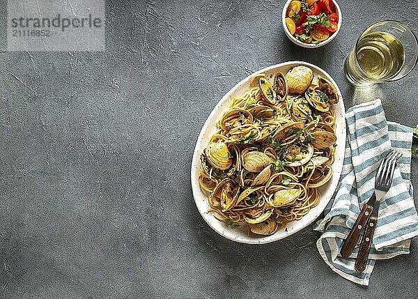 Nudeln mit Meeresfrüchten. ITALIENISCHE SPAGHETTI ALLE VONGOLE. Spaghetti mit Venusmuscheln auf weißem Teller mit Weißwein  grauer Hintergrund. Ansicht von oben