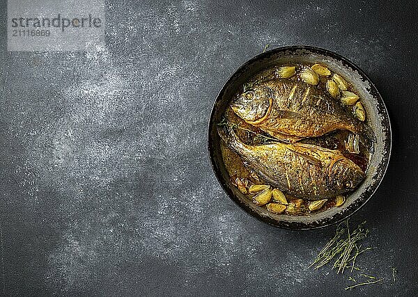 Gebackene Dorade mit Zwiebeln und Kräutern in der Pfanne auf dunklem Hintergrund